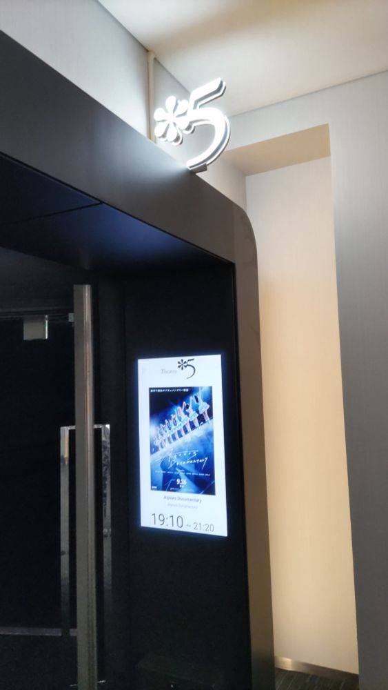 新宿ピカデリー館内、『AqoursDocumentary』上映スクリーン入り口。電子掲示板にポスターが投影されている。