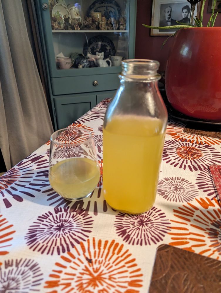 Partially filled wine glass and bottle of dandelion wine, translucent orange in colour.