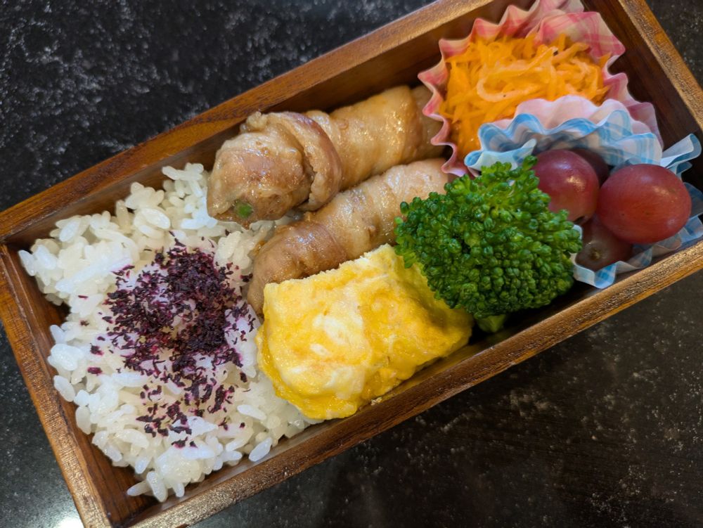 木の四角いお弁当箱にゆかりごはん、ししとう肉巻き、チーズオムレツ、ブロッコリー、にんじんラペ、ぶどう