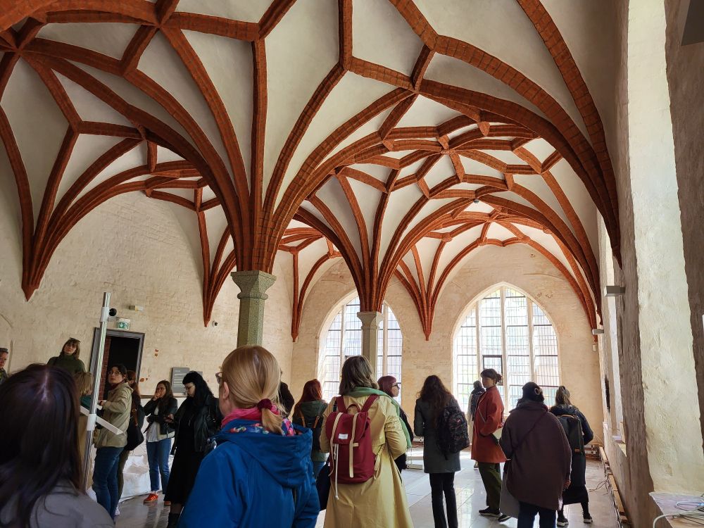 Inside the cloister of Stralsund, group of people under a red brick gothic vault 