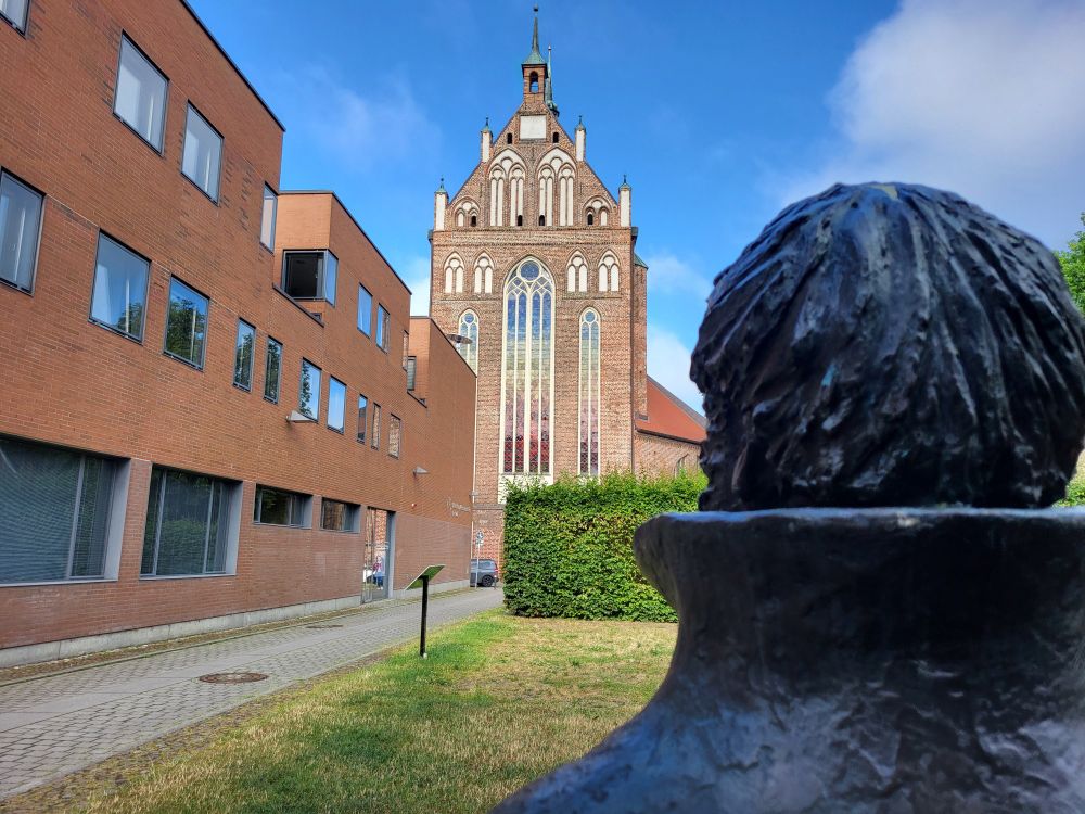 Blick auf den Ostchor von St. Nikolai in Greifswald, links das Alfried Krupp-Wissenschaftskolleg, rechts Rückenfigur von Bronzestatue Caspar David Friedrichs