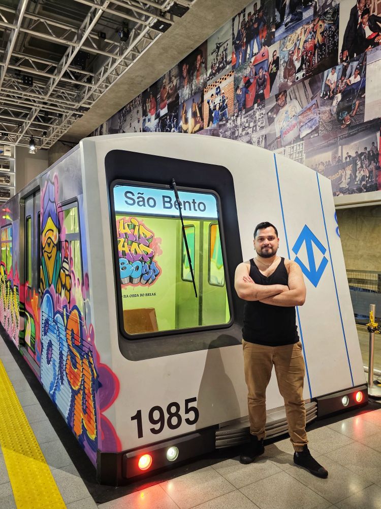 Uma gay de regata na frente de um metrô cenográfico grafitado. 