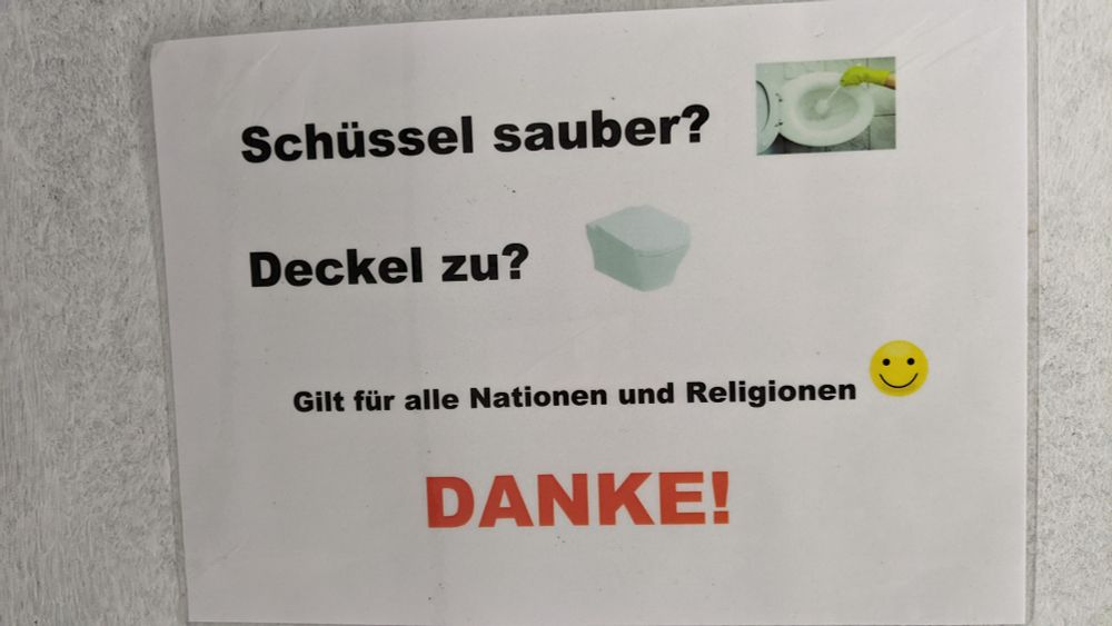 Aushang in einem öffentlichen WC: "Schüssel sauber? Deckel zu? Gilt für alle Nationen und Religionen. Smiley. DANKE!"