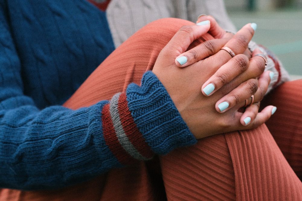 Two hands clasp a knee. The model is wearing a cabled sweater with stripes at the cuff. This sweater is set to be released as a knitting pattern called Forty Love.