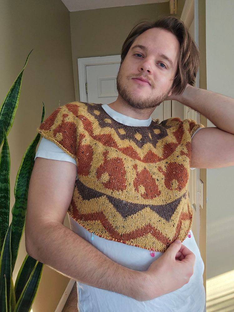 A man is wearing a yellow, brown, and red circular yoke sweater that is completely through the underarm and a proportion of the body is worked.