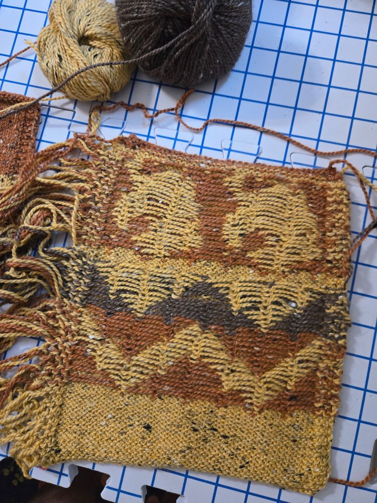 The wrong side of a stranded colorwork knitted swatch worked in tweed yarns in yellow, orange, and brown.