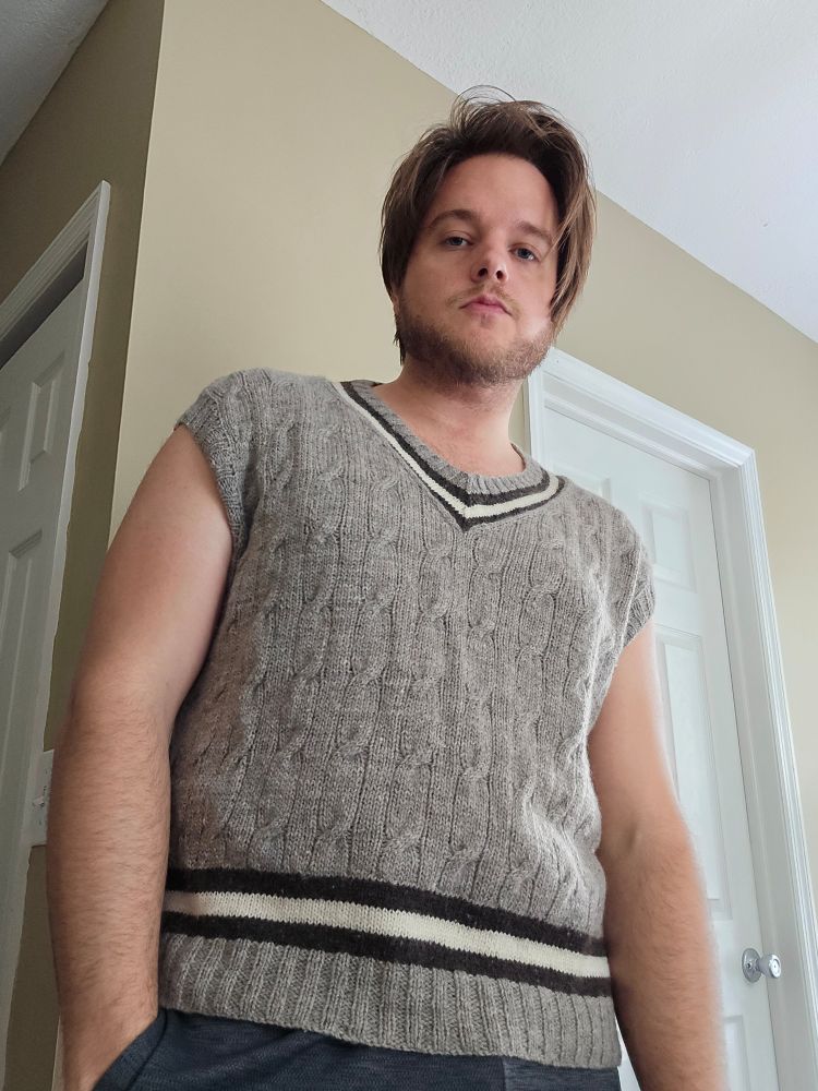 A man wears a cabled tennis sweater vest in undyed yarn