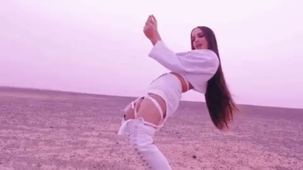 a woman is dancing in the desert wearing a white outfit and white boots .