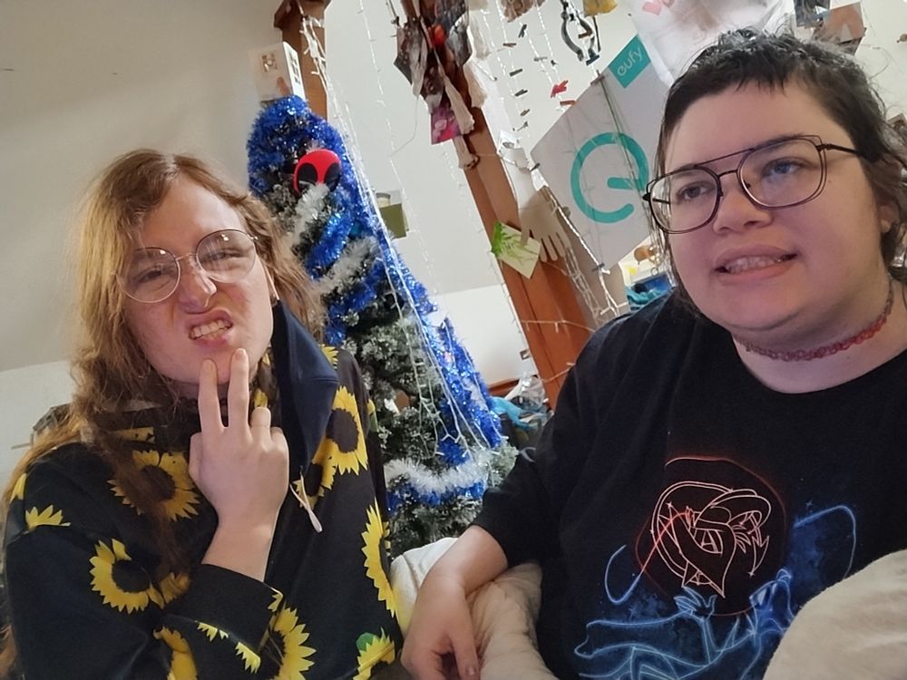 2 dorks in glasses smiling funny and a Christmas tree behind them