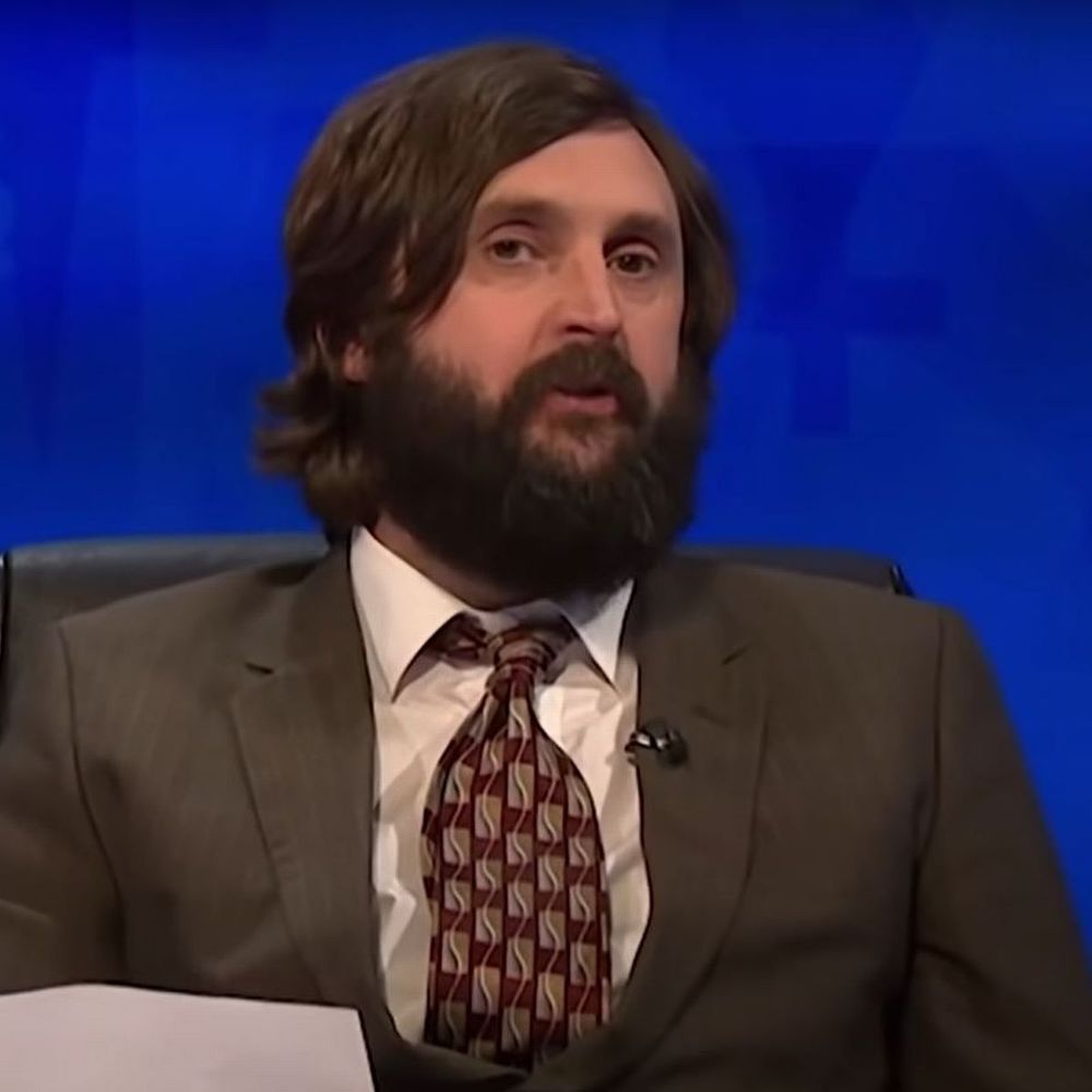 Joe Wilkinson in a suit, looking like a scruffier Slavoj Žižek