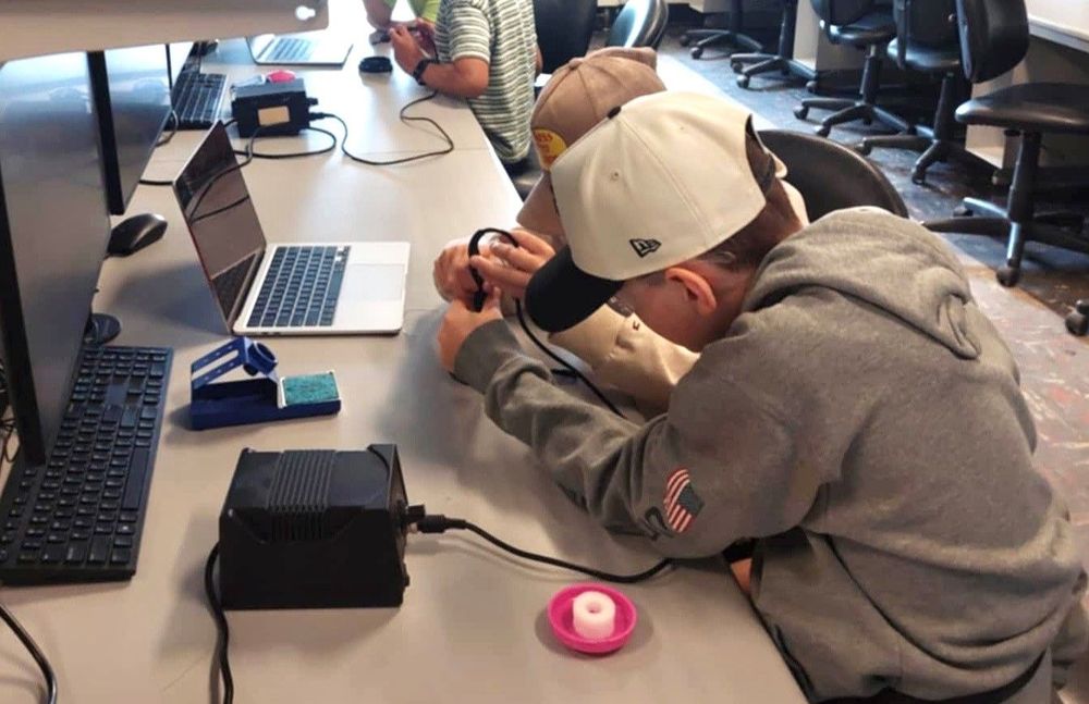 Young students work on a device together at a build event.