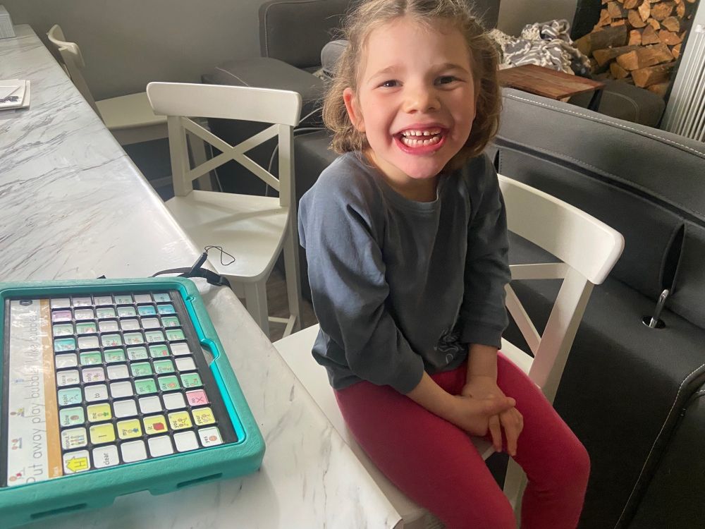 Natasha's daughter smiling with her TouchChat and keyguard on top.