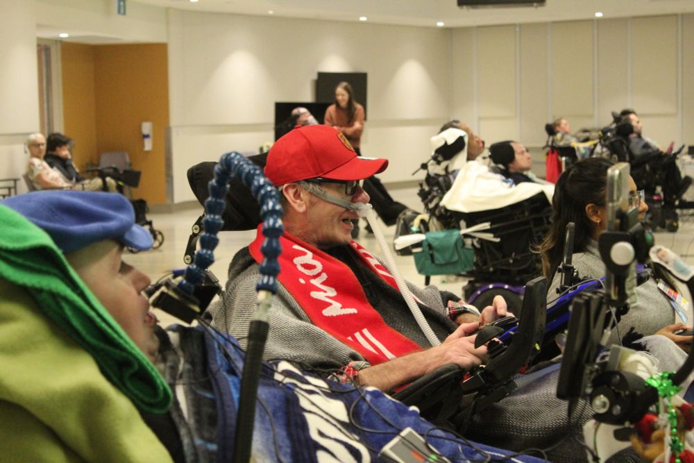 A man in a wheelchair plays FIFA 2023 by using his tongue with a mounted joytick against another man in a wheelchair.
