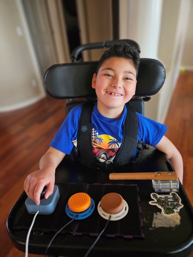 Adam in his wheelchair, with joysticks and switches on his lap tray to play video games.