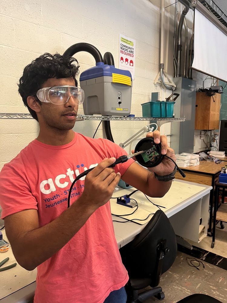 Anshul, wearing safety glasses, uses a soldering iron to work on a device.