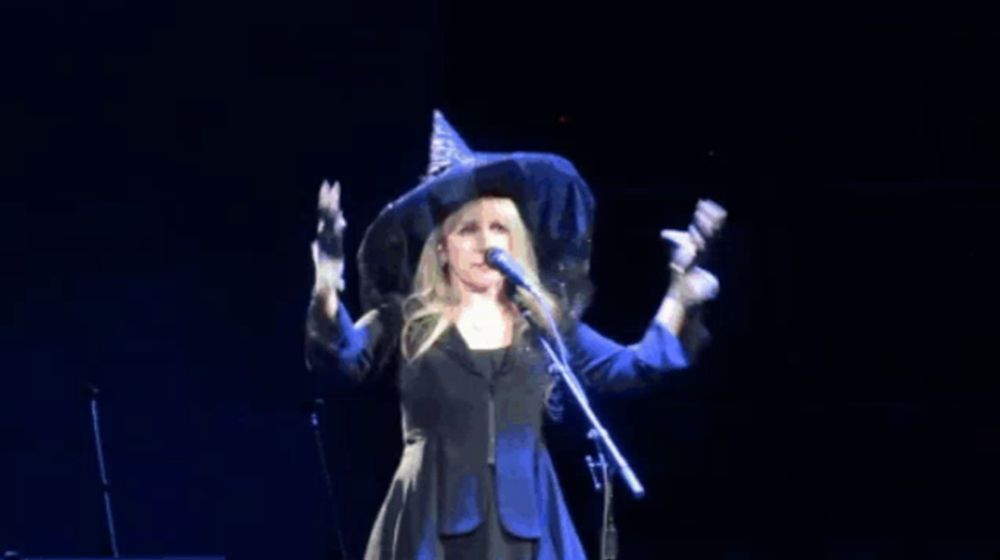 a woman in a witch hat sings into a microphone