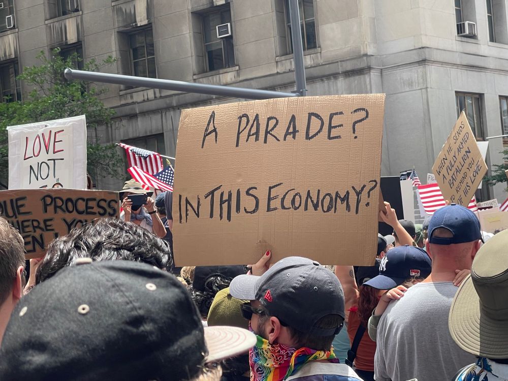 Sign on Brian cardboard that reads: “A parade? In this economy?”