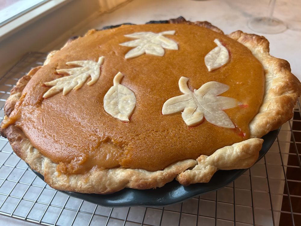 A pumpkin pie on a cooling rack. Decorated on top with fall leaf shapes.