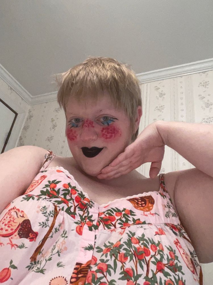 White nonbinary person in funky polka dot, rosy makeup and a chicken printed pink nightgown.  