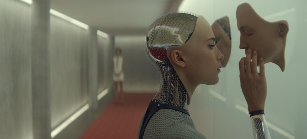An android with a human face touching a disembodied, human-like face on a wall. Still from the film Ex Machina - BagoGames/Flickr.
