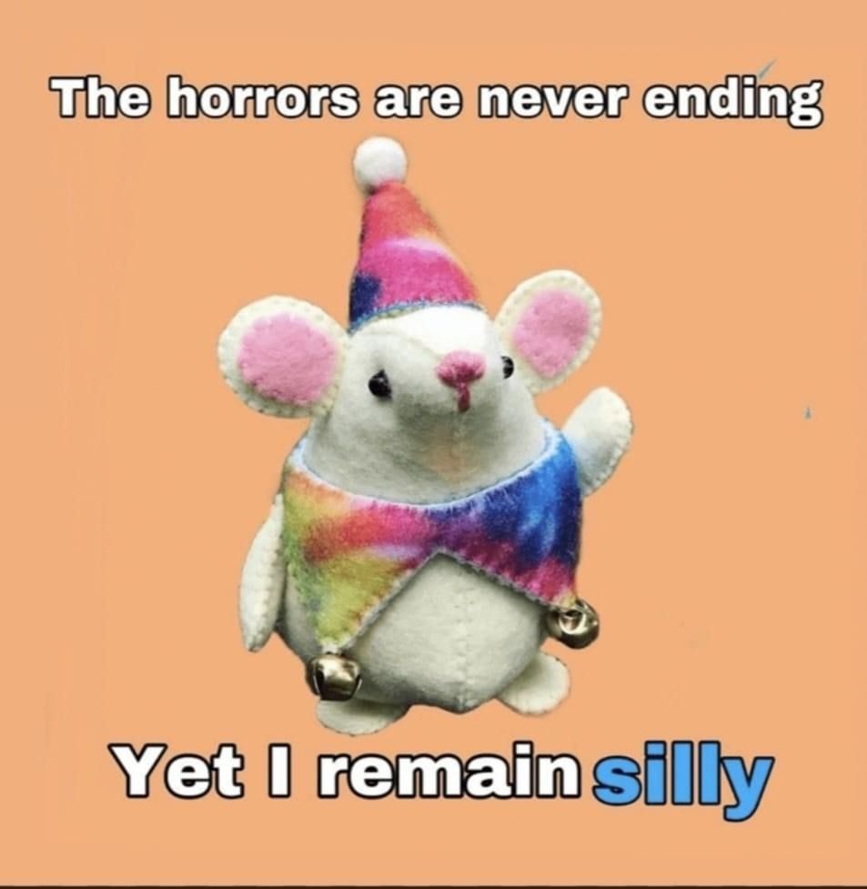 a plushie of a mouse wearing a silly multicolored pointy hat with a ball on top and a multicolored top with two bells attached and the text "the horrors are never ending, yet i remain silly"