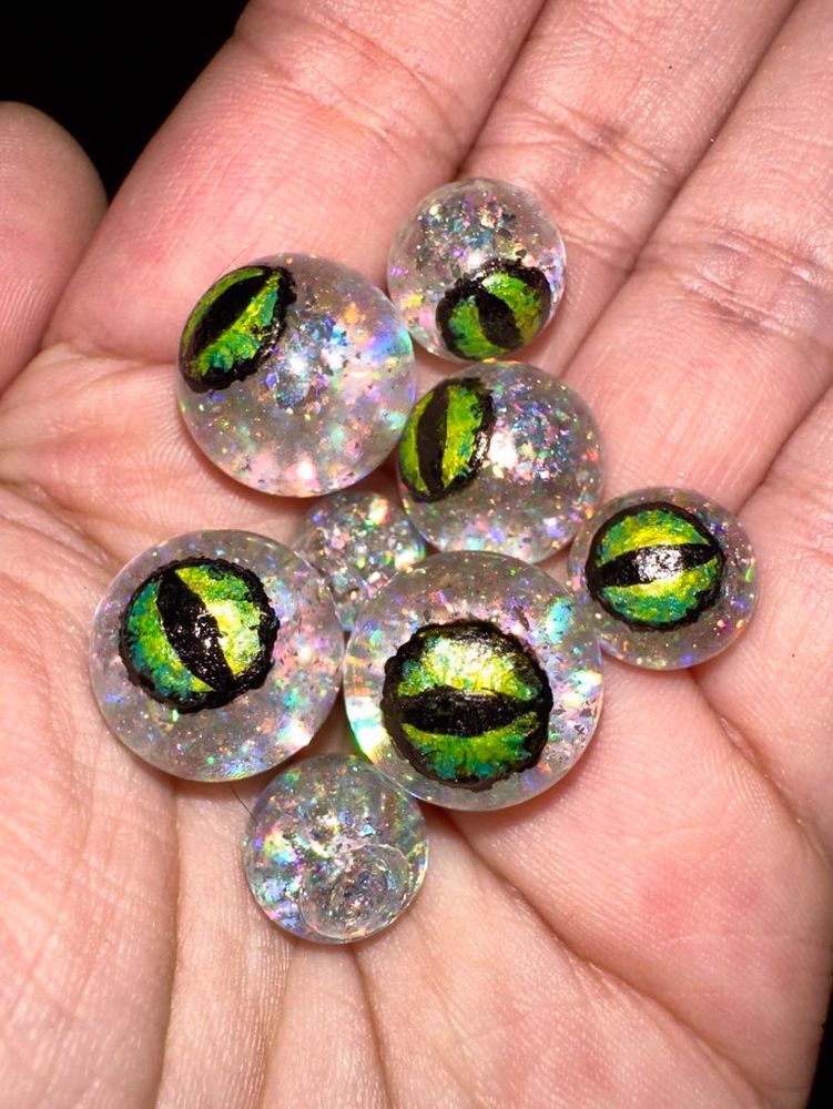 a handful of glittery liquid cores for dice, hand painted with green dragon’s eyes