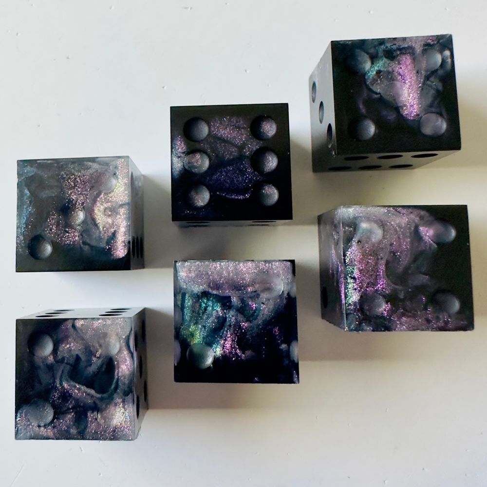 Six pip d6 dice that are black with swirls of shimmery rainbow color shifting glitter. The dice are unfinished and uninked.