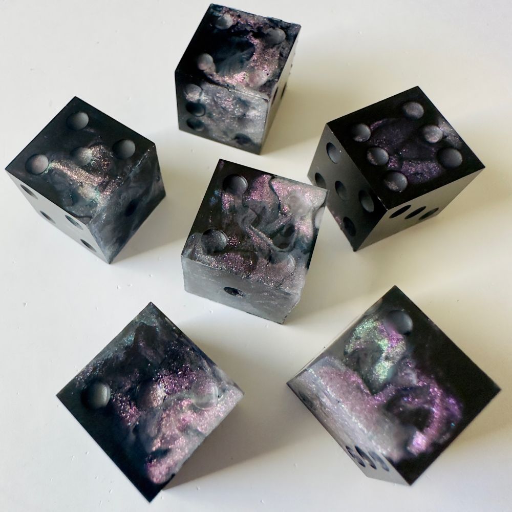 Six pip d6 dice that are black with swirls of shimmery rainbow color shifting glitter. The dice are unfinished and uninked.
