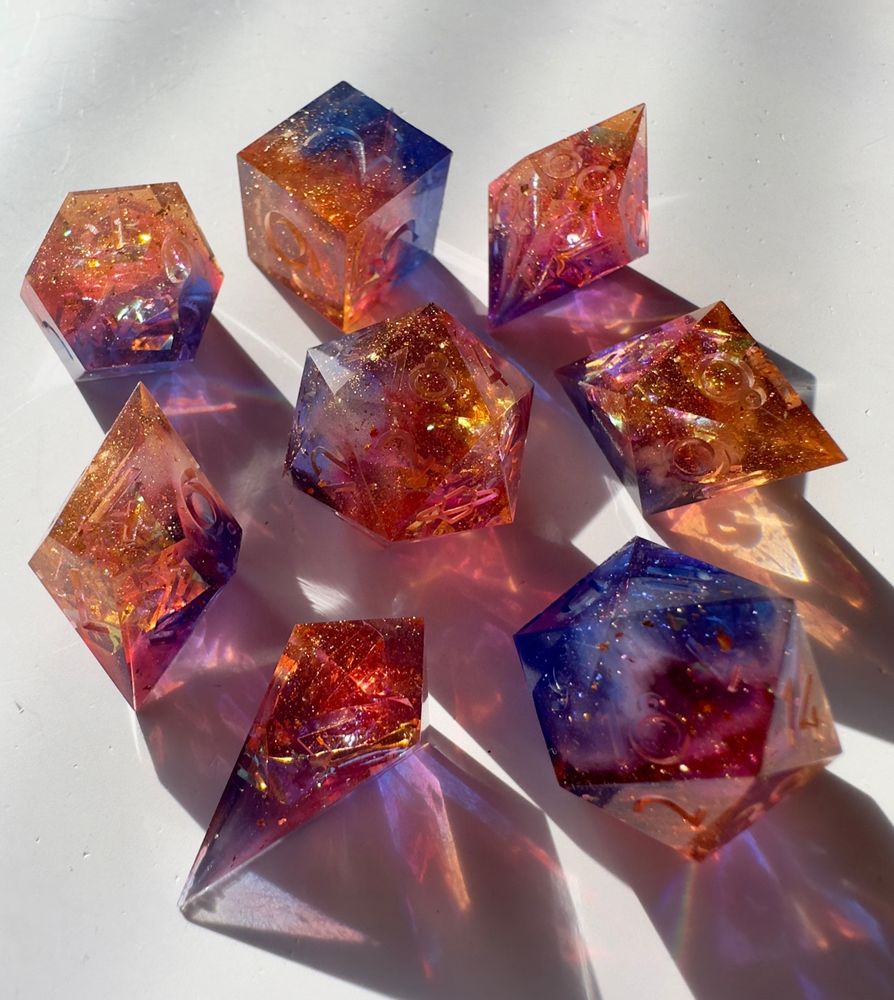 A dice set inspired by the previous image, in a gradient of orange, red, and blue with glitter and holographic mylar inside.