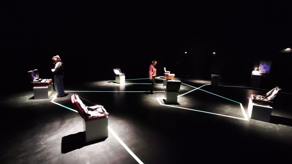 schwarzer Raum in dem wenige Sockel mit Koffern drauf angestrahlt sind