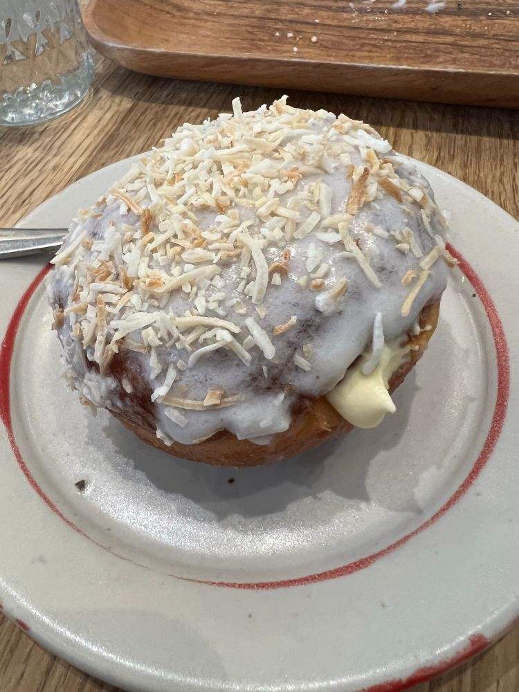 Filled donut with passionfruit whipped cream and topped with coconut glaze and streusel on a plate