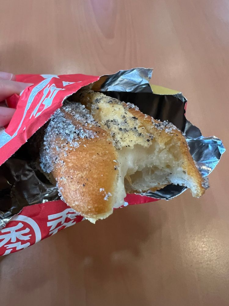 Chinese donut stuffed with mochi covered in black sesame sugar with a bite taken out of it and held in a foil bag
