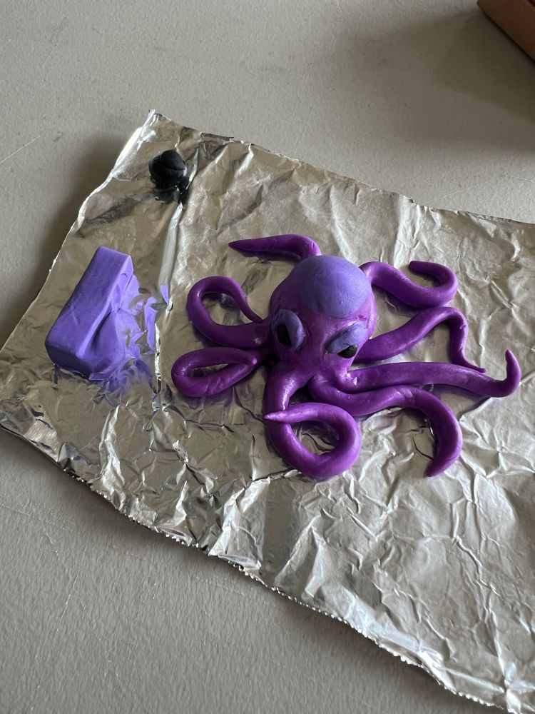 Clay sculpture of purple octopus on a piece of foil with chunks of unused clay next to it