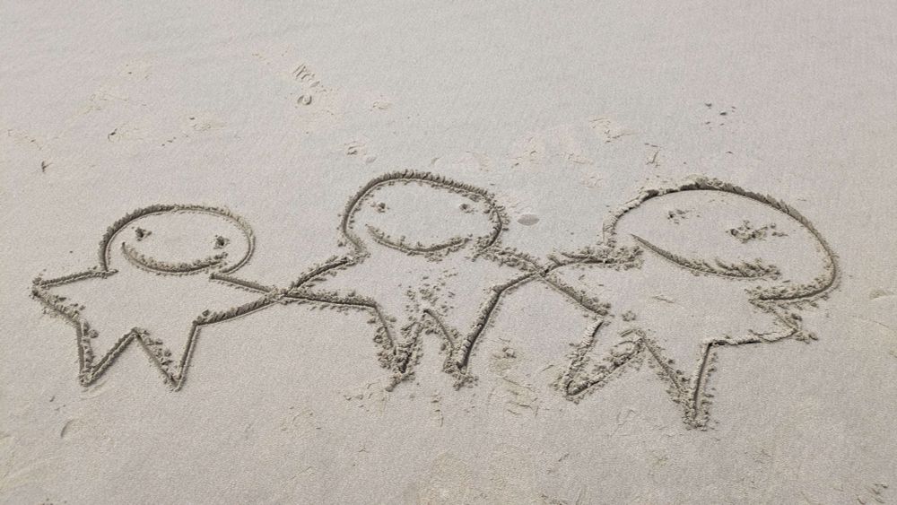 three oings, progressively more crude in construction. they are all holding hands. medium is beach sand