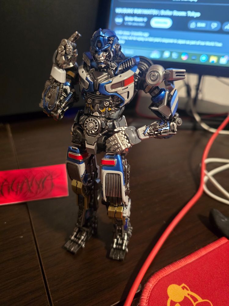 A photo of the same figure, standing with his left hand on his hip, making a salute with his right arm.