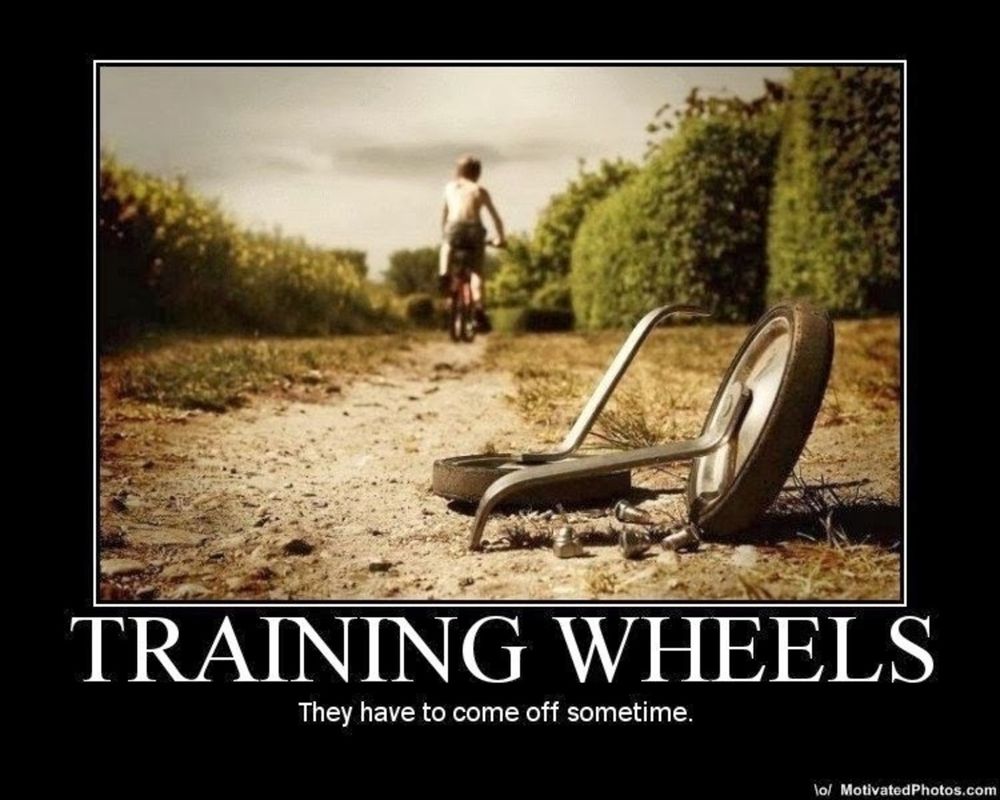A child rides a bike without training wheels along a countryside path, while the removed training wheels lie discarded in the foreground with the caption TRAINING WHEELS: They have to come off sometime.