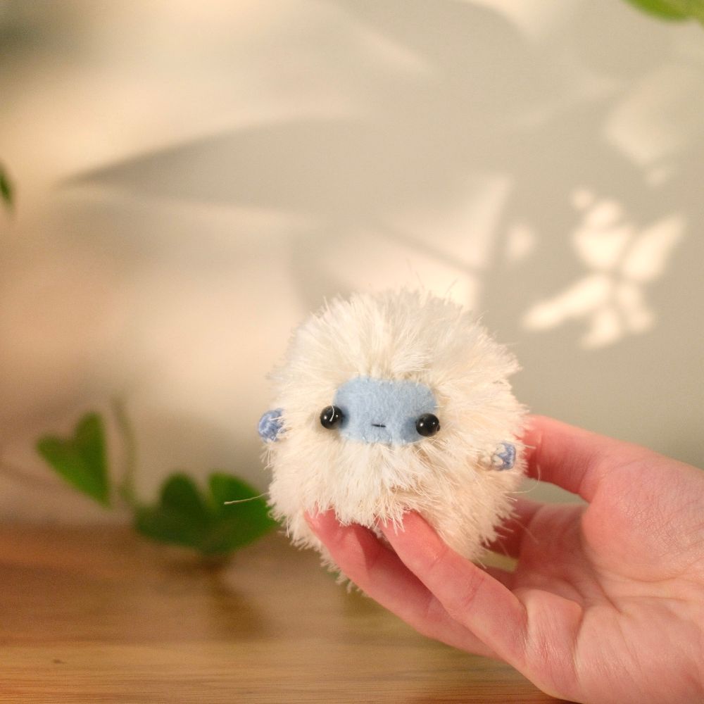 A hand holding a fluffy white yeti plush with a blue felt face