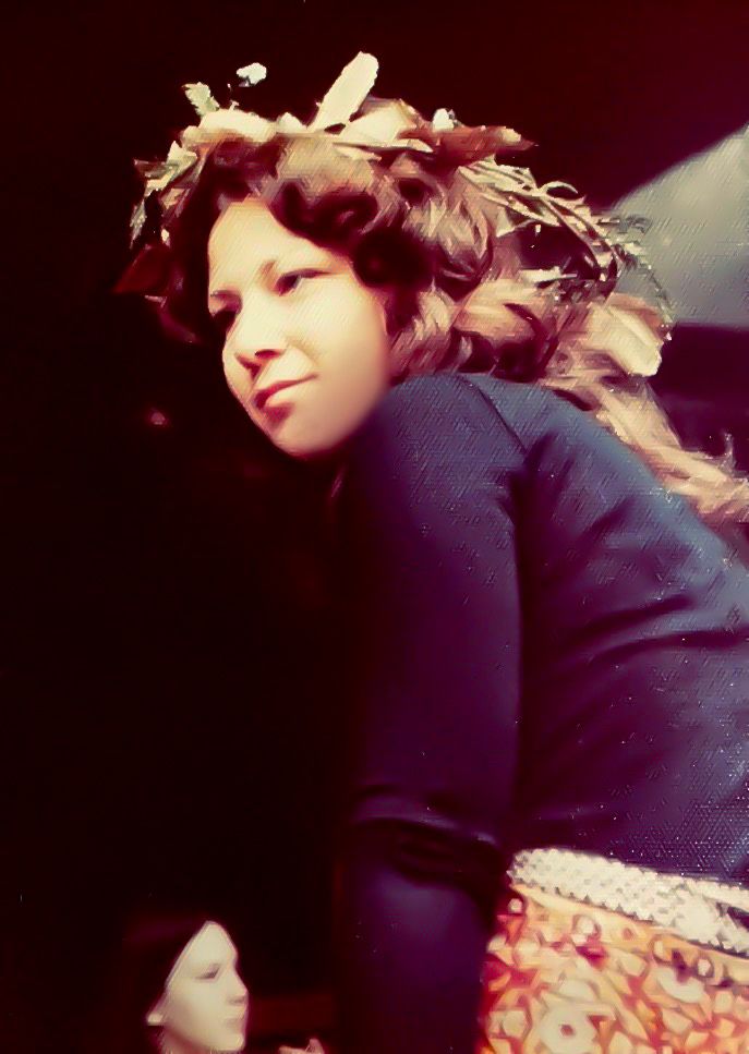 A favorite photo of my mom, back in the late 1970’s at the Asilomar in Pacific Grove, California. She wears a dark blue sweater, a skirt, and a wreath of flowers in her hair. 
