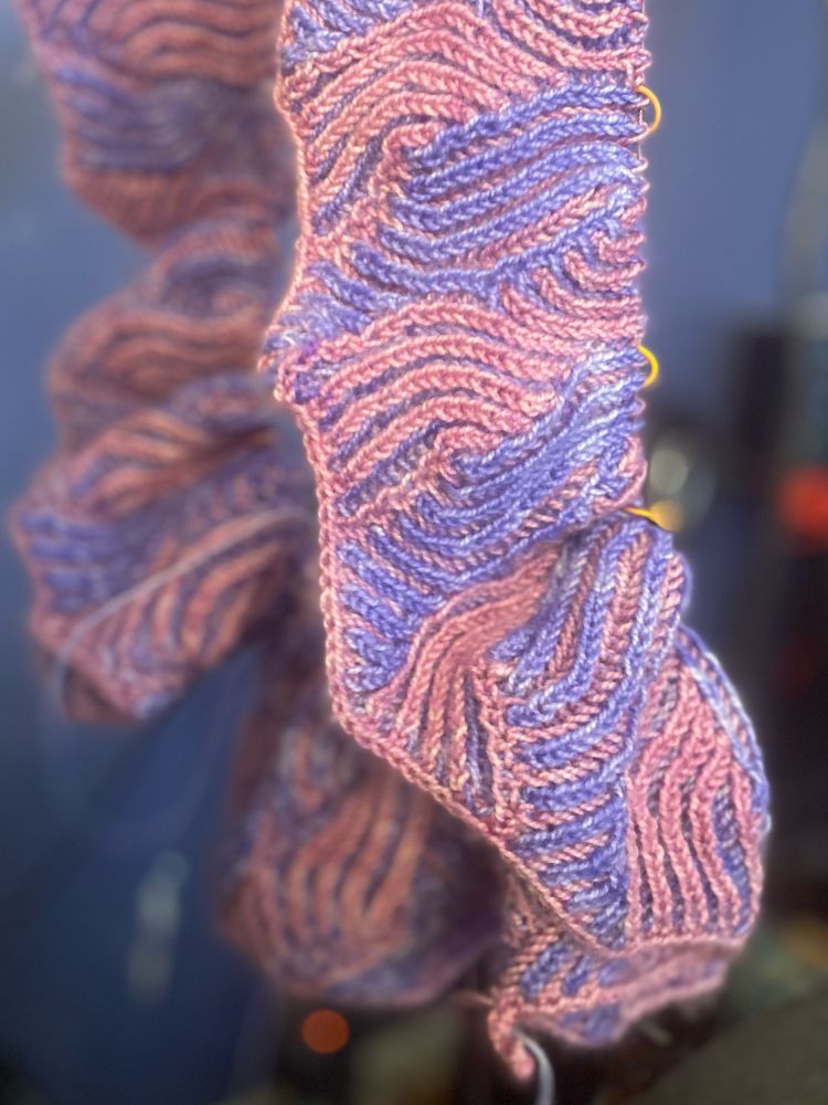 An unfinished knitted cowl in periwinkle and pink.
