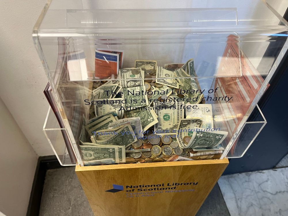 perspex box on wooden stand, with many coins and notes inside