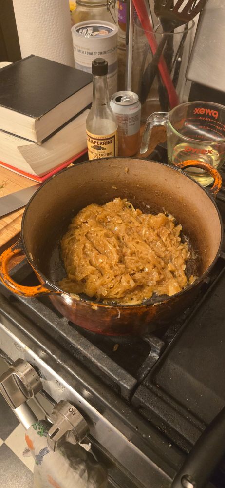 An orange pot on the stove with a mass of golden onions inside. 