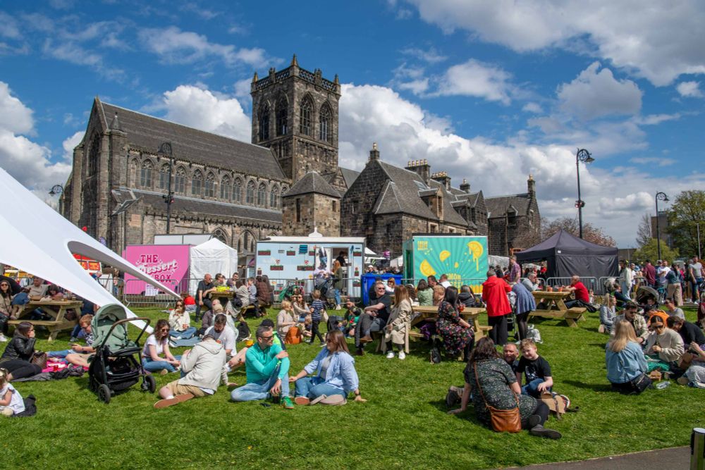 People relaxing outside on the grass at Paisley Food and Drink Festival with Paisley Abbey in the background. 