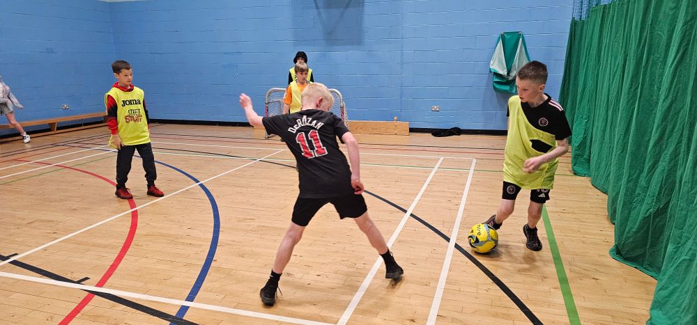Four children play football in a gym hall.