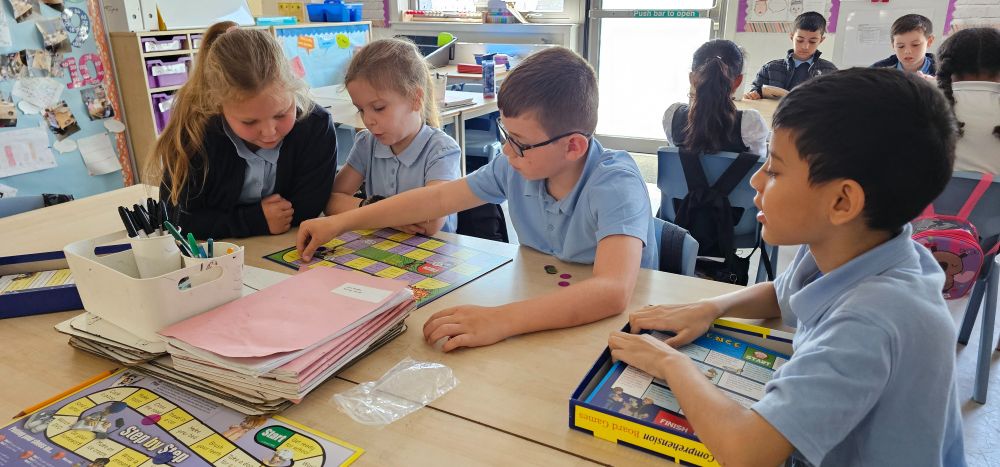 Four pupils play an educational board game at a desk.