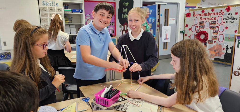 Four pupils work together to make a structure out of straws. Two are smiling.