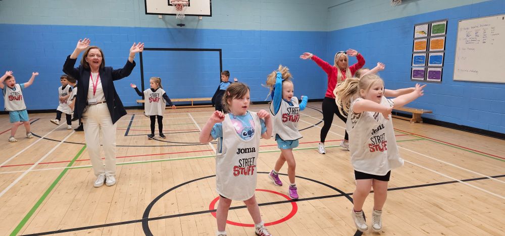 Children and adults dance in a gym hall.