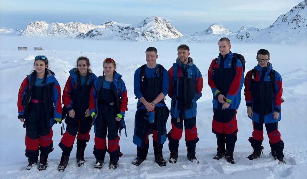 Seven pupils wearing insulated jumpsuits stand in a snowy field.