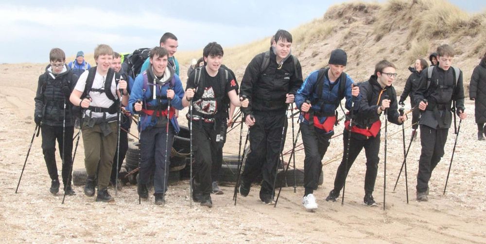 More than 10 pupils pull tyres across a sandy beach as part of training for pulling sledges on snow.