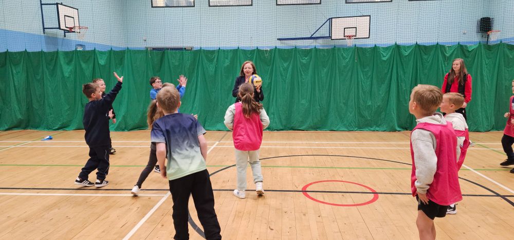 Children and adults play hand ball in a gym hall.