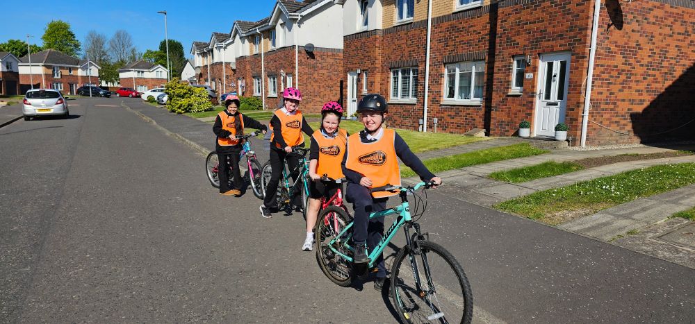 Four pupils on bikes, wearing orange hi-vis vest and safety helmets.